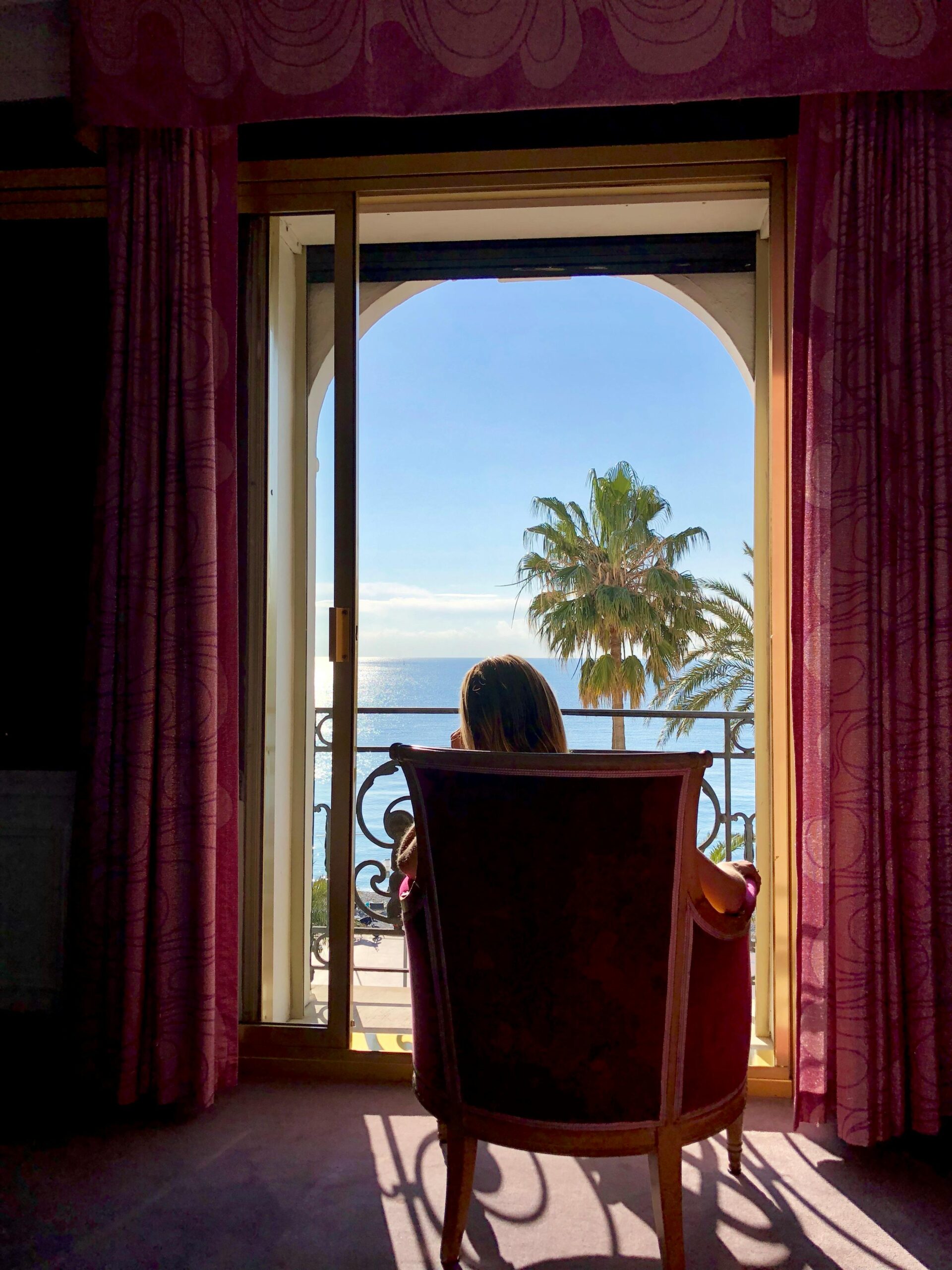 Woman seated in a luxury hotel room overlooking the sea and palm trees through balcony doors
