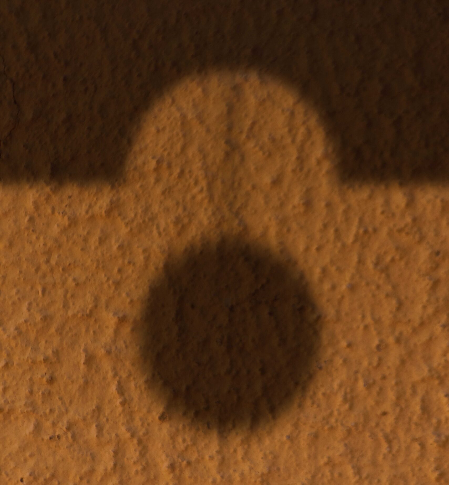 Shadow of a dome and a circular shape cast on a textured building wall.