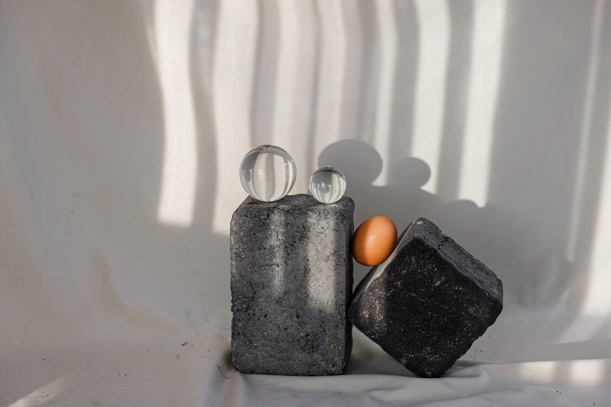 Two square stone pedestals with transparent and orange glass marbles arranged in a balanced composition.