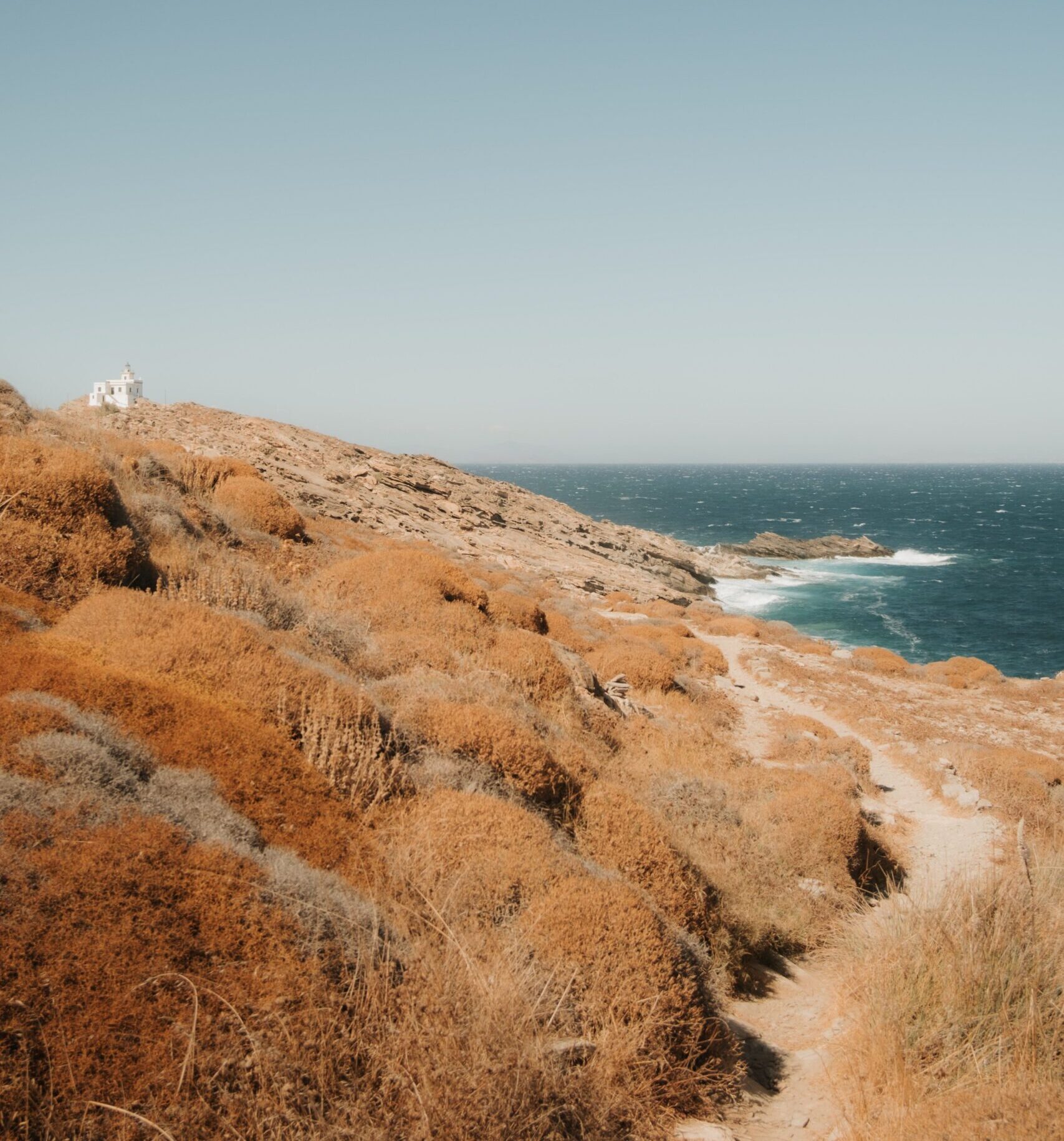 A winding coastal road curves alongside a rugged shoreline beneath an open sky.