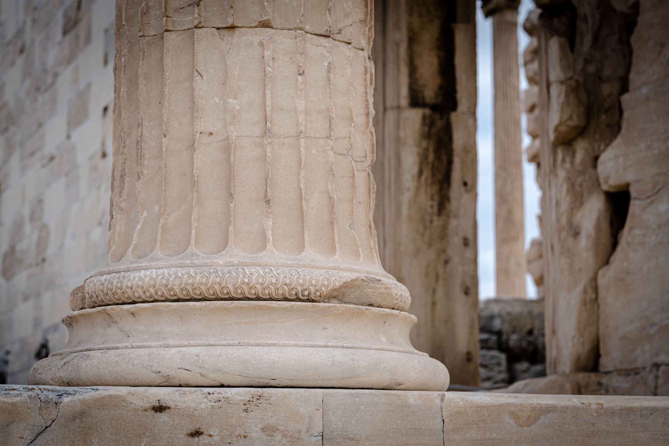 Detail of an ancient marble temple showing the base of a weathered column against a bright sky.