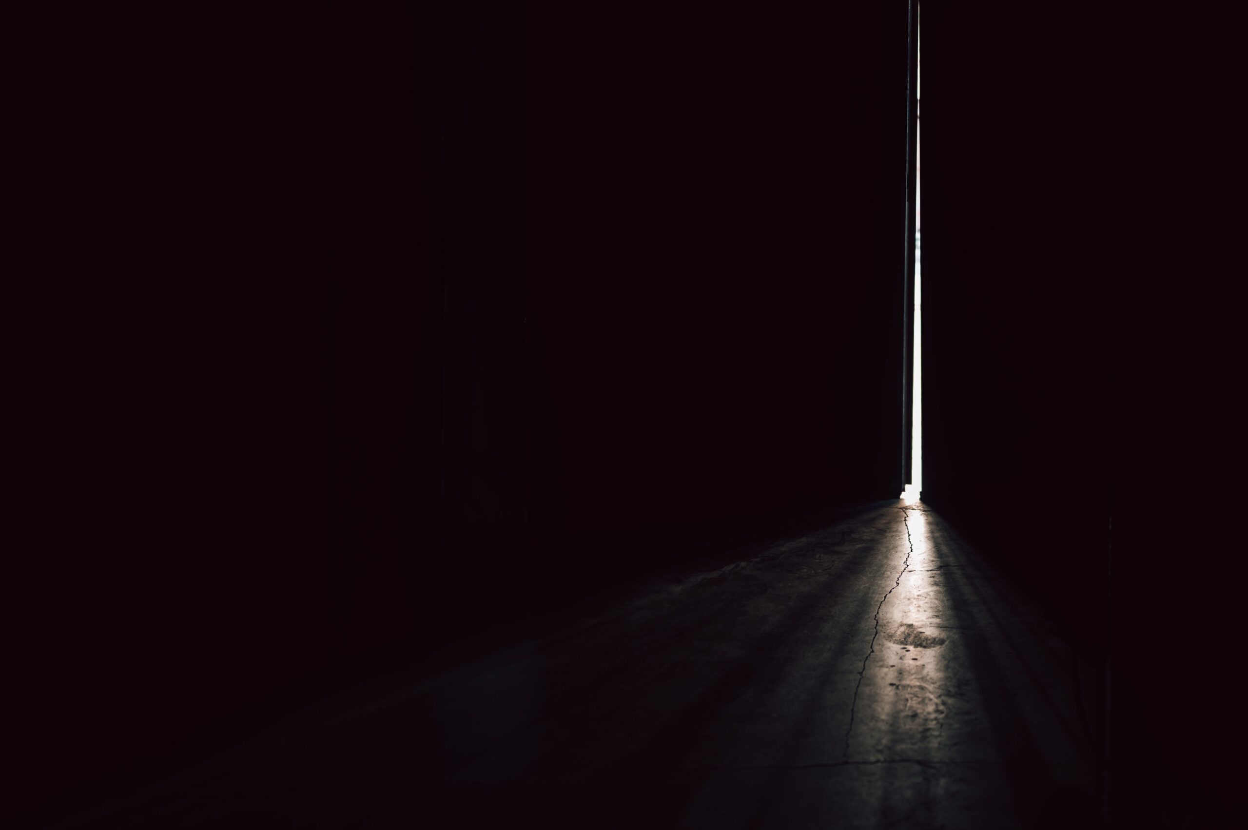 Dark architectural door casting a beam of white light that reveals a crack in the floor
